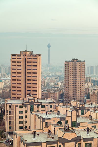 برج میلاد بین دو آسمان خراش در خط افق تهران که با درخشش گرم نارنجی غروب آفتاب روشن شده است