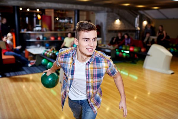 مفهوم مردم اوقات فراغت ورزش و سرگرمی - مرد جوان خوشحال در حال پرتاب توپ در باشگاه بولینگ