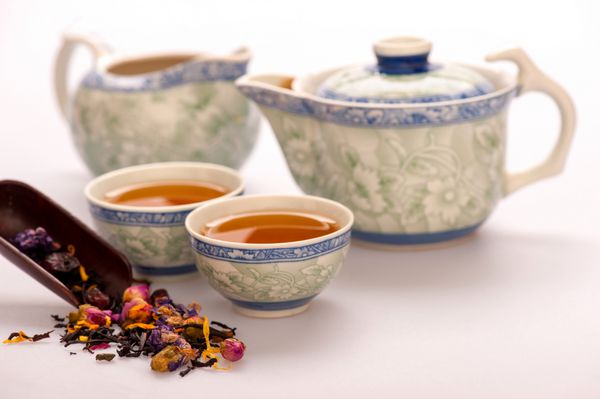 خانه جایی است که چای است ترکیب زیبای قوری و فنجان های سنتی چینی سفالی احاطه شده با چای گلدار جدا شده در پس زمینه سفید با فوکوس انتخابی
