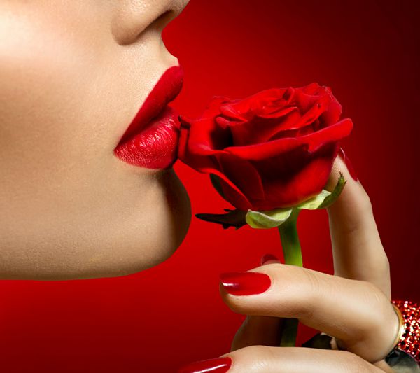 زن مدل زیبا در حال بوسیدن گل رز قرمز لب قرمز ناخن و گل رز دختر زیبایی آرایش و مانیکور دهان حسی لب های قرمز رنگ خیابان طراحی روز بخشی از f