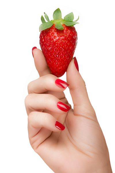 دست زن را با ناخن های بسیار زیبا با لاک ناخن قرمز در دست بگیرید و توت فرنگی خوش رنگ را در تناسب رنگ با مفهوم رژیم غذایی سالم و تمیز در زمینه سفید جدا کنید