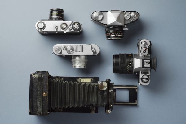 مجموعه ای از دوربین های قدیمی و لنز دوربین به خوبی در پس زمینه آبی نمای بالا سازماندهی شده است