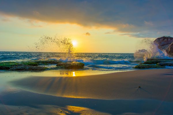 غروب آتشین خورشید در یک ساحل ساحلی مدیترانه ای در شرق میانه امواج بر روی s های رنگارنگ می پاشند و آسمان کمی ابری است
