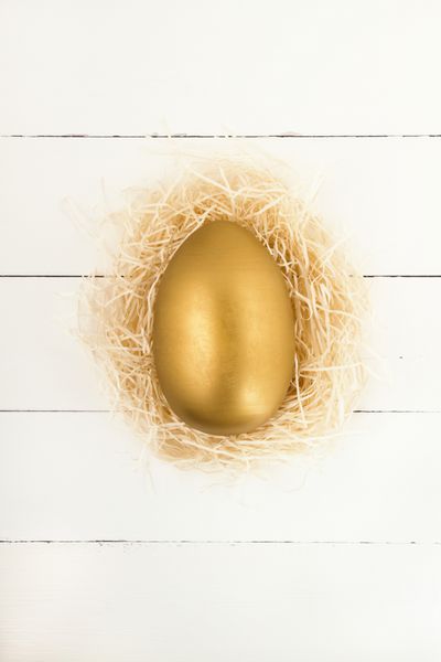 تخم مرغ طلایی عید پاک در لانه در پس زمینه چوبی سفید