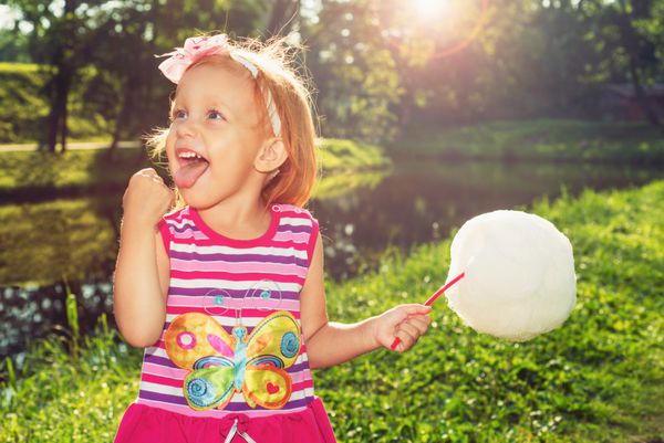 دختری شاد در حال خوردن آب نبات پنبه ای در طبیعت