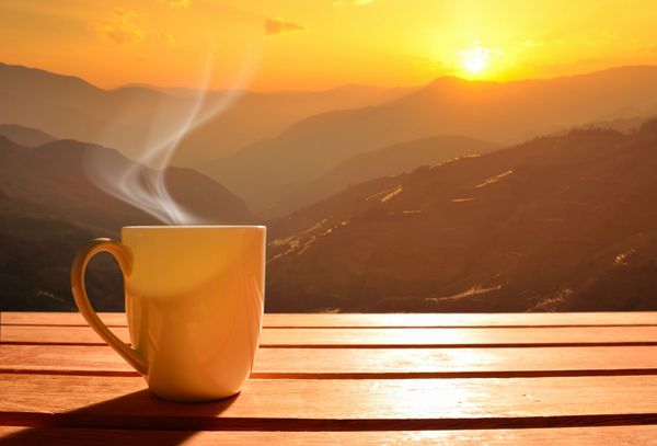فنجان قهوه صبحگاهی با پس زمینه کوه در طلوع خورشید