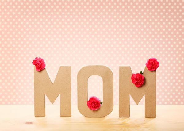 متن سه بعدی مادر با گل های میخک تازه ایستاده روی میز چوبی با پس زمینه خال خال صورتی