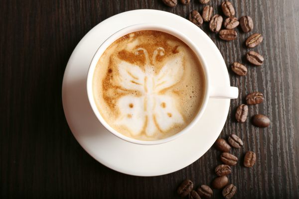 فنجان قهوه لاته آرت با دانه های روی زمینه چوبی