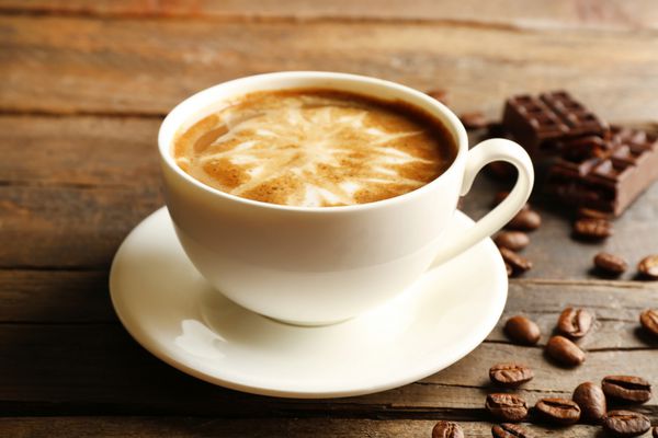 فنجان قهوه لاته آرت با دانه ها و شکلات در زمینه چوبی