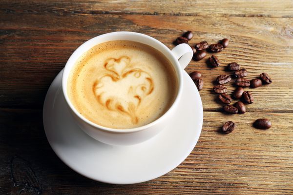 فنجان قهوه لاته آرت با دانه ها در پس زمینه چوبی