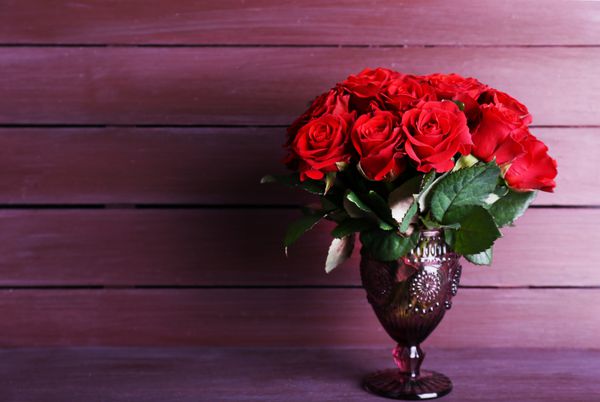 دسته گل رز قرمز در گلدان شیشه ای در زمینه چوبی
