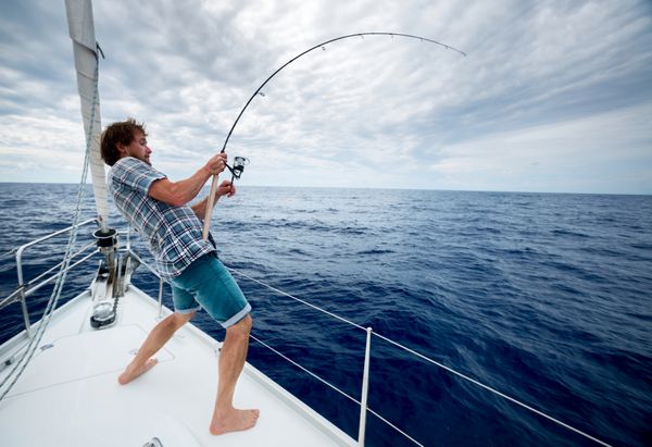 مرد جوانی که از قایق بادبانی در دریای آزاد ماهیگیری می کند
