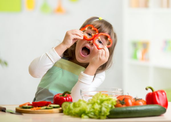 دختر بچه در حال سرگرمی با سبزیجات غذا در آشپزخانه