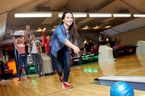 مفهوم مردم اوقات فراغت ورزش و سرگرمی - زن جوان شاد در حال پرتاب توپ در باشگاه بولینگ