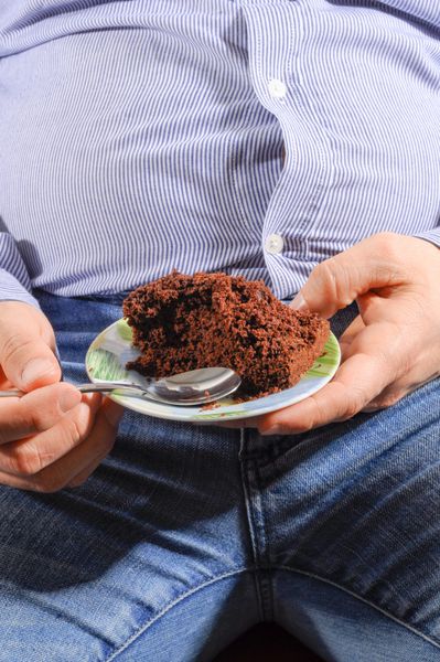 دست های بزرگ و شکم در حال خوردن یک کیک شکلاتی