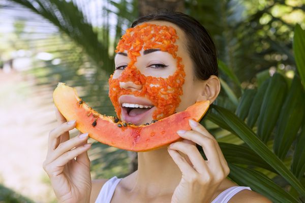 زن زیبای قفقازی با استفاده از ماسک صورت طبیعی پاپایای میوه تازه مراقبت از پوست و سلامتی آنتی اکسیدانی ماسک ویتامین صورت تکه های پاپایا در سالن اسپا در فضای باز غذای عجیب و غریب سالم