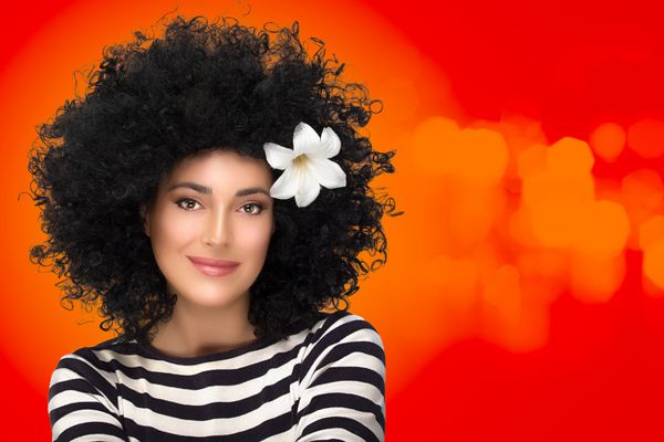 مراقبت از مو زیبایی پرتره زن مدل مد با مدل موی آفروی مجعد سالم و گل زنبق در مو پرتره مد روی پس زمینه نارنجی و قرمز با کپی sp