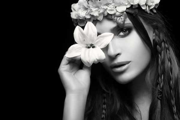 زیبایی در مفهوم بهار زنی زیبا که یک زنبق بهاری را روی یک چشم خود نگه داشته و مدل موهایش تاجی از گل است پرتره تک رنگ زیبایی جدا شده روی مشکی با کپی sp برای متن