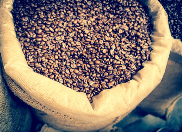 دانه های قهوه بو داده به سبک رترو نمای بالا گونی بزرگ با قهوه برشته شده با افکت فیلتر اینستاگرام قهوه سیاه در رنگ وینتیج با فوکوس ملایم