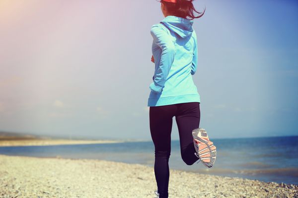دونده ورزشکار در حال دویدن در ساحل سنگی مفهوم تناسب اندام زن تمرین دویدن در حال تندرستی
