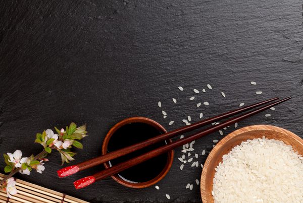 چاپستیک سوشی ژاپنی روی کاسه سس سویا برنج و شکوفه ساکورا در زمینه سنگ سیاه نمای بالا با copy sp