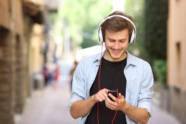 پسر خوشحال راه می رود و از تلفن هوشمند برای گوش دادن به موسیقی با هدفون استفاده می کند