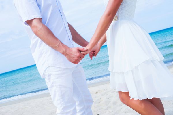 زوج عاشق در حال قدم زدن و در آغوش گرفتن در ساحل گرمسیری تابستانی