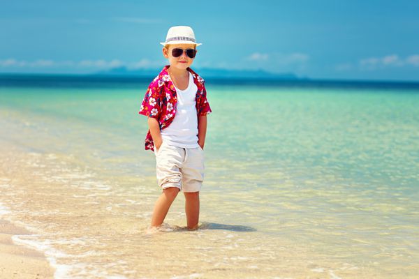 پسر زیبا و شیک در موج سواری در ساحل تابستانی ایستاده است