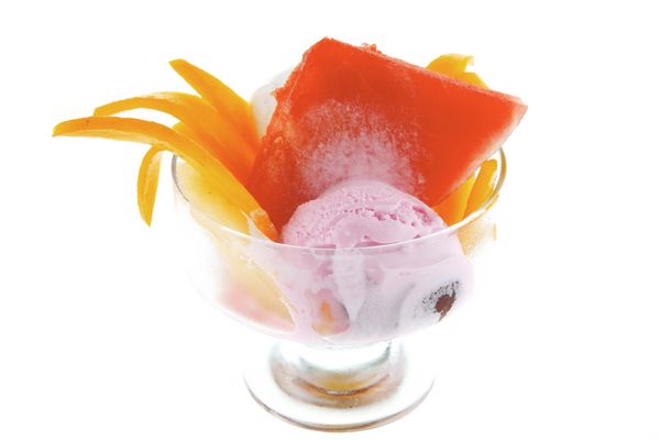 فنجان شیشه ای کوچک شفاف با بستنی و میوه های گرمسیری جدا شده در زمینه سفید