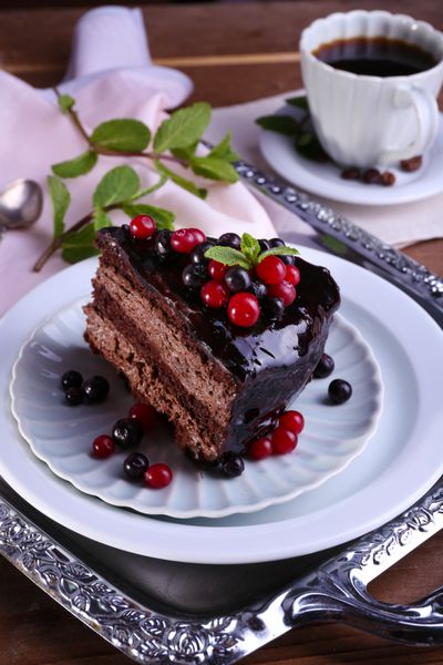 کیک شکلاتی خوشمزه با انواع توت ها و فنجان قهوه روی میز