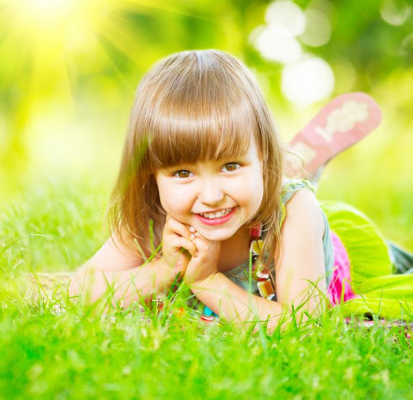 پرتره دختر کوچک لبخند بر روی علف سبز دراز کشیده است کودک ناز سه ساله از طبیعت در فضای باز لذت می برد بچه سالم و بی دغدغه بیرون در پارک تابستانی بازی می کند فضای متن خود را کپی کنید