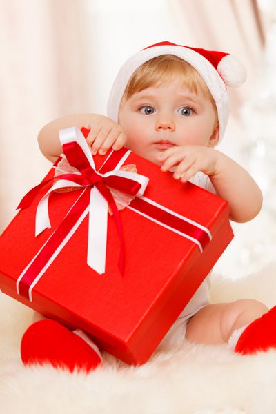 بچه سانتا یک جعبه هدیه قرمز بزرگ در دست دارد