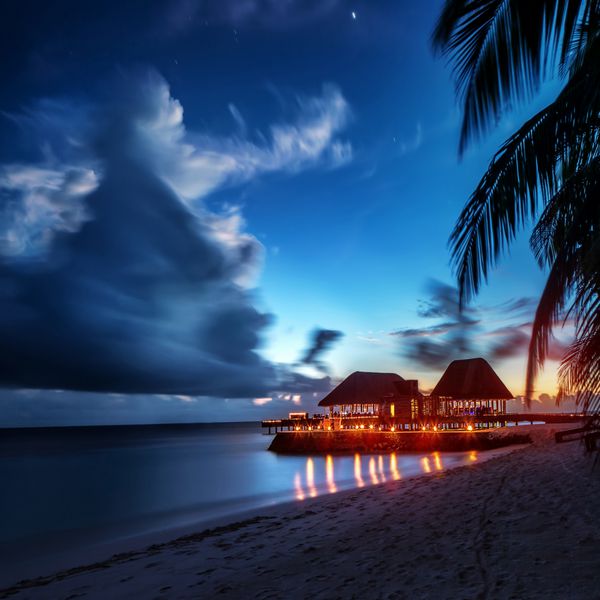 ساحل بهشتی در شب نور درخشان در رستوران روی آب مکانی عاشقانه برای تعطیلات ماه عسل عصر تابستانی در جزیره عجیب و غریب چشم انداز مالدیو