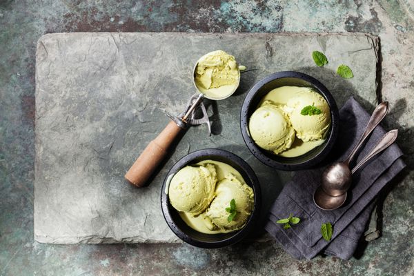 بستنی چای سبز با برگ های نعناع و قاشق بستنی در زمینه سنگ تخته سنگ