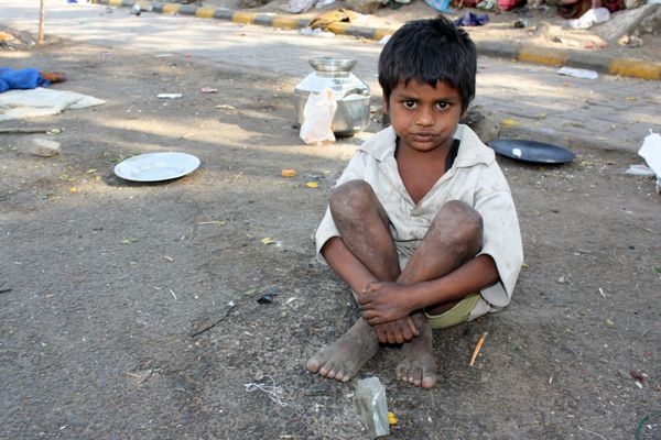 یک بچه فقیر در هند کنار خیابان نشسته است