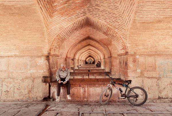 اصفهان ایران - 15 اکتبر پیرمردی با دوچرخه خود رمانی را در زیر پل معروف خواجو در 15 اکتبر 2014 خواند نمونه خواسته معماری ایرانی پل خواجو توسط شاه عباس دوم در سال 1650 ساخته شد