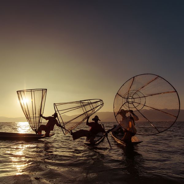 ماهیگیر برمه ای با قایق بامبو در حال صید ماهی به روش سنتی با تور دست ساز دریاچه اینله مقصد سفر میانمار برمه