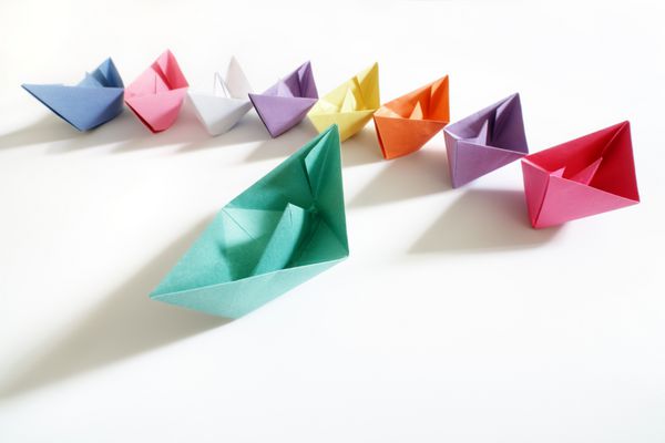قایق های کاغذی چند رنگ به دنبال یک مفهوم قایق رهبر برای رهبری کار گروهی و موفقیت