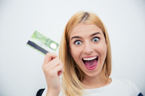 زن جوان شاد کارت بانکی را در پس زمینه خاکستری در دست دارد