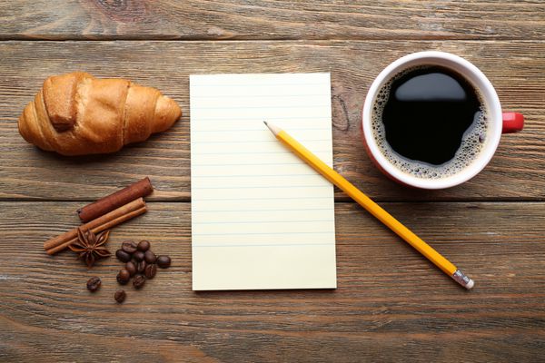 فنجان قهوه با ورق کریسانت تازه و کاغذ خالی کاغذ بر روی میز چوبی نمایش بالا
