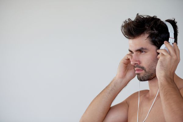مرد جوان خوش تیپ در خانه مدرن روی دیوار سفید موسیقی گوش می کند و روی دست ایستاده است
