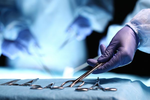 دست پرستاری که قصد جراحی را برای گروهی از جراحان در بستری بیمار جراحی در تئاتر جراحی می گیرد ذرات پزشکی فولادی آماده استفاده مفهوم جراحی و اورژانس