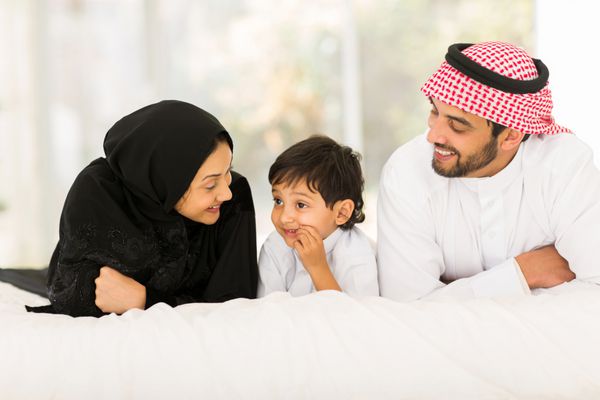 خانواده سه نفره مسلمان جوان شاد که روی تخت در خانه دراز کشیده اند