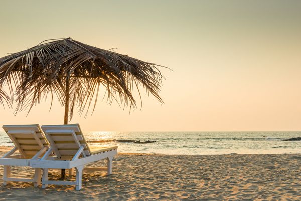 صندلی های خالی زیر چترهای کاهگلی در ساحل شنی