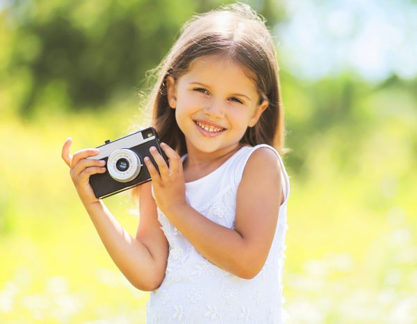 پرتره آفتابی کودک دختر کوچک خندان و بامزه با دوربین قدیمی قدیمی در روز تابستان