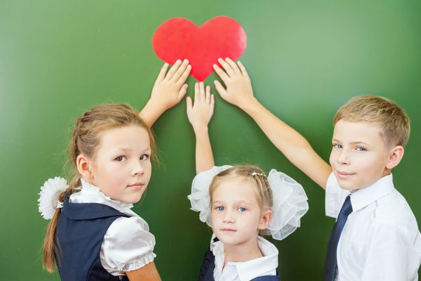 بچه های شاد مدرسه یا بچه هایی که نماد قلب را در کلاس مدرسه نزدیک تخته سیاه در دست دارند آنها به دوربین نگاه می کنند آموزش عشق به مدرسه به کودکان بسیار مهم است به مدرسه خوش آمدید