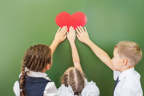 بچه های شاد مدرسه یا بچه هایی که نماد قلب را در کلاس مدرسه نزدیک تخته سیاه در دست دارند آموزش عشق به مدرسه به کودکان بسیار مهم است به مدرسه خوش آمدید
