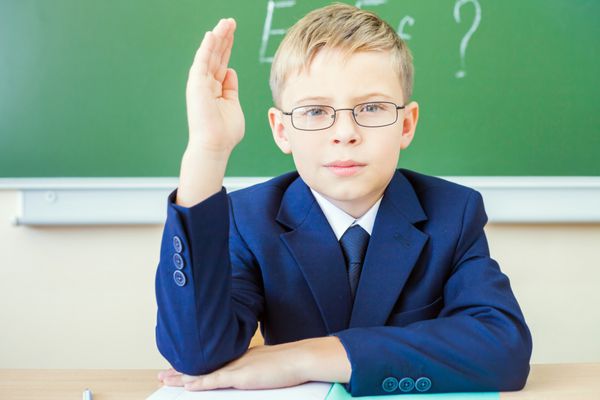 پسر مدرسه ای که لباس مدرسه و عینک پوشیده بود آماده پاسخگویی بود و دستش را بلند کرد مفهوم ایده و دانش برای آموزش ابتدایی آموزش برای آینده فرزندان ما بسیار مهم است