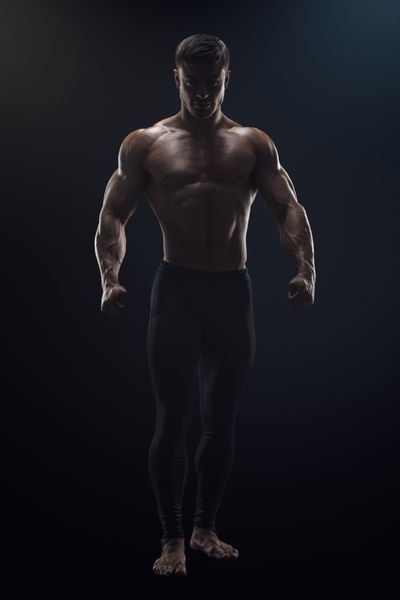 تصویر یک بدنساز قوی بدون پیراهن که برای تمرین آماده می شود مفهوم دراماتیک یک مرد جوان با اعتماد به نفس تناسب اندام با عضلات اصلی دستان قدرتمند و مشت های گره کرده