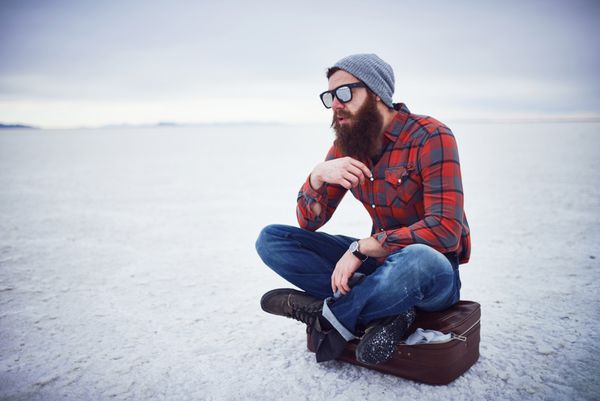 هیپستر متفکر و متفکر نوازش ریش مردانه فوق‌العاده و نشسته روی چمدان قدیمی در نمک‌دان به تنهایی با ترکیب کپی sp